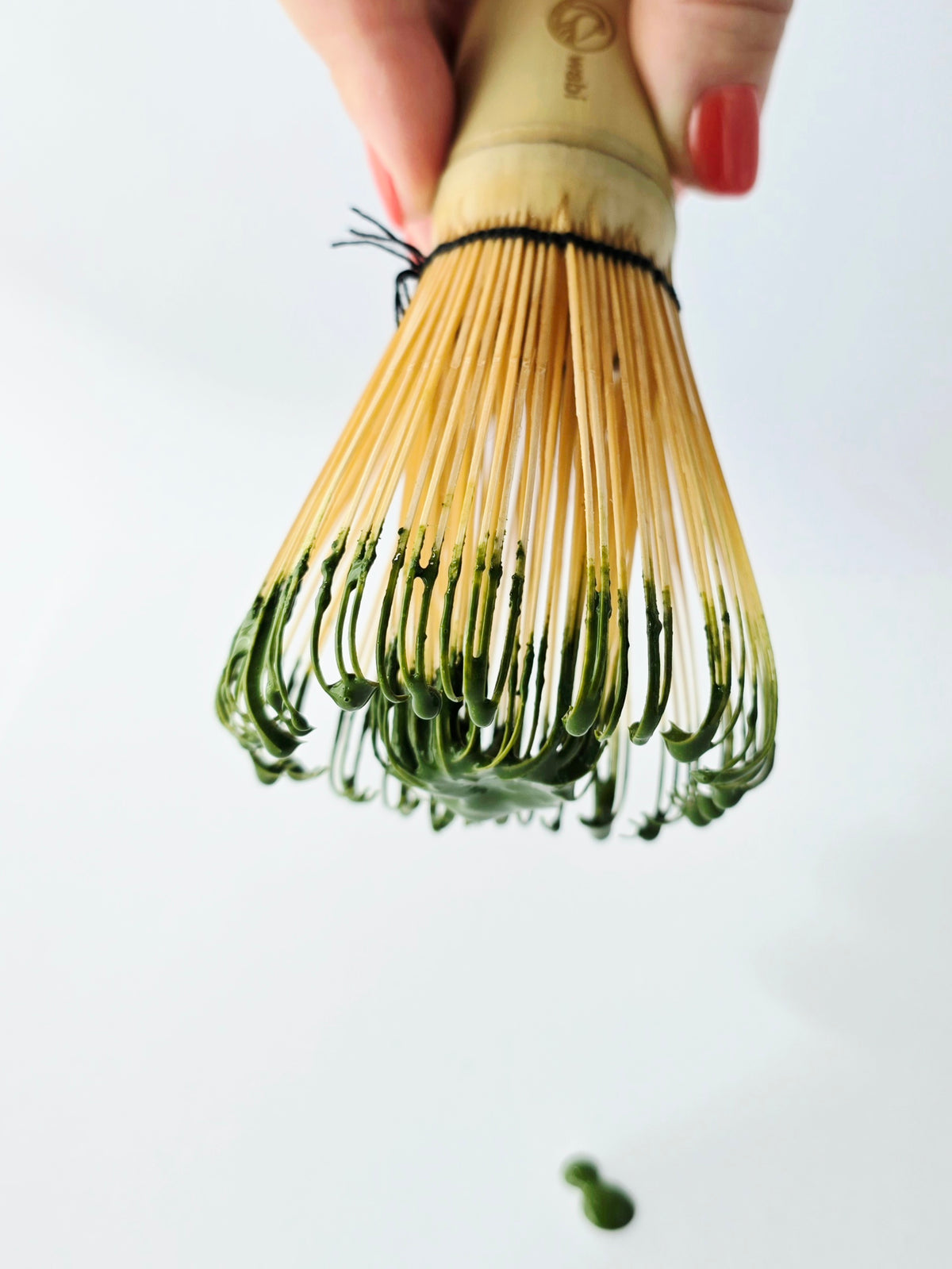 Wabi Cafe Matcha on a bamboo whisk held by female hand with red nails on a white background