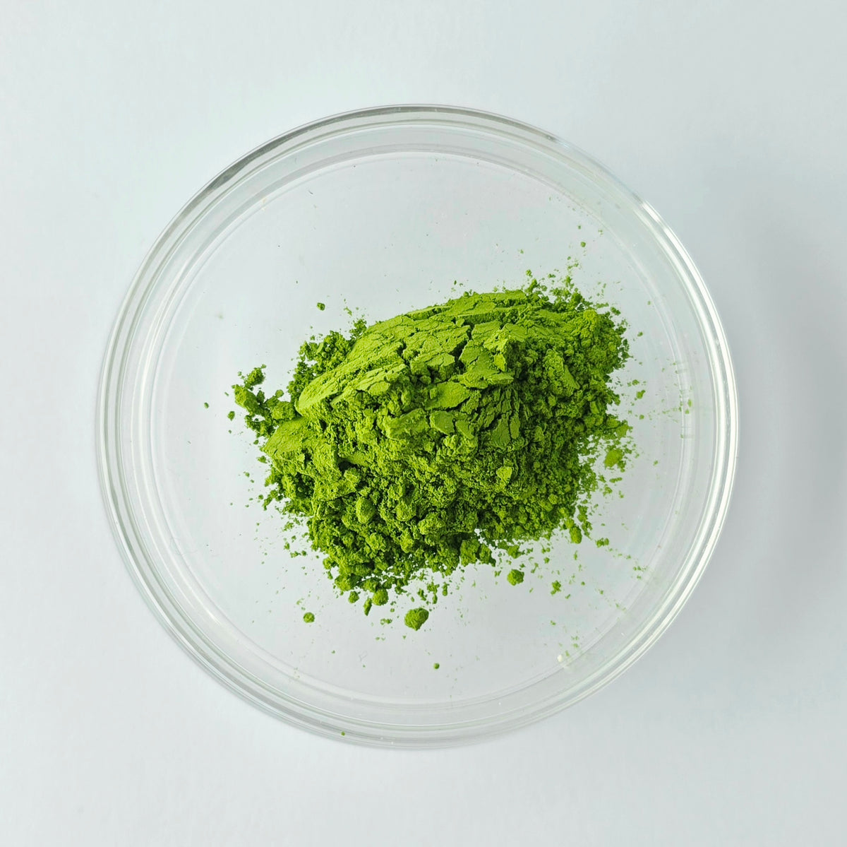 Green powder in a clear glass bowl on a white background